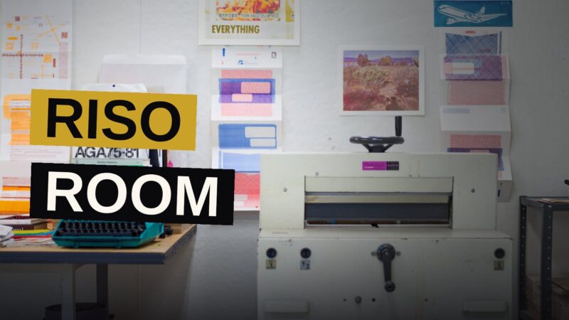 An artist dances while folding and binding books in a sunlit print studio.
