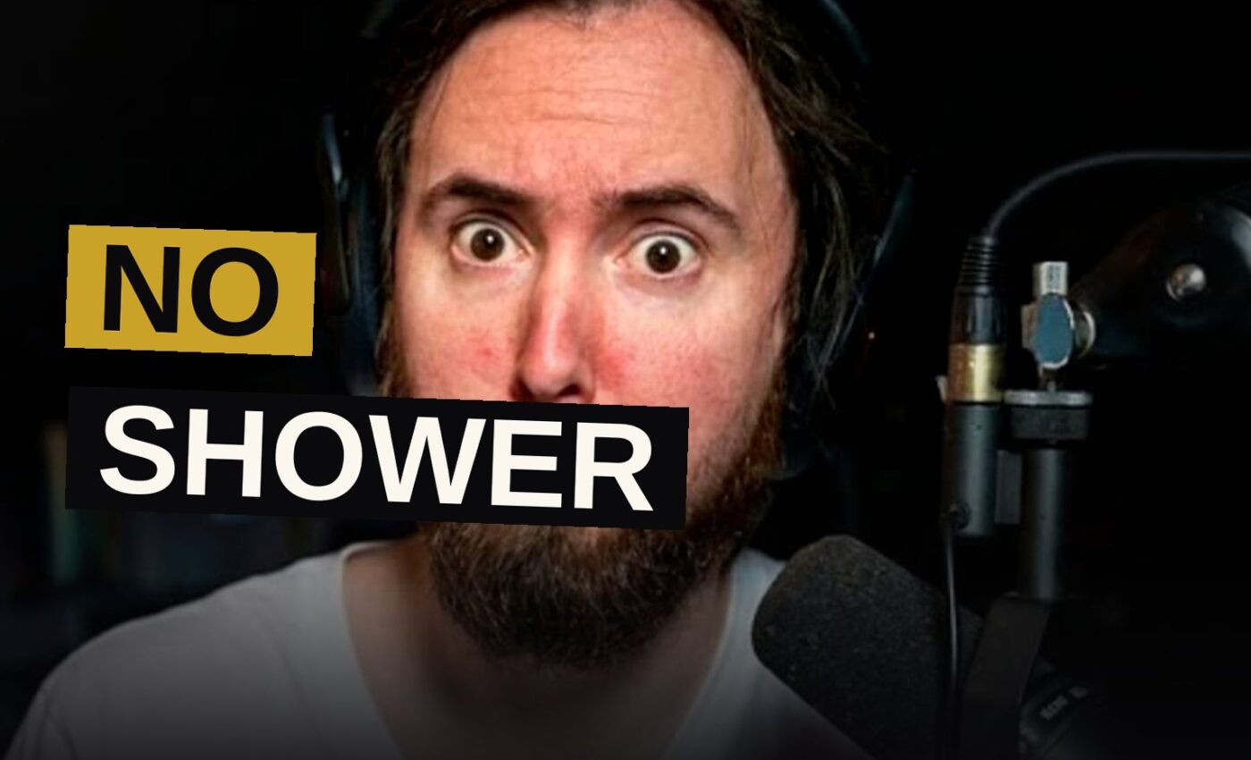 Asmongold sits at his gaming desk with messy hair, looking unbothered, in a dimly lit room with RGB lighting.