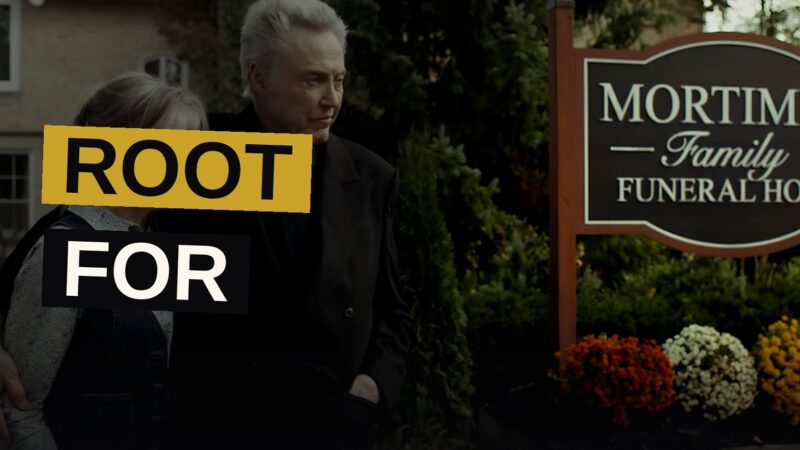 An old man and a young woman stand silently together in a dim funeral home, evoking a tale of dread and affection.