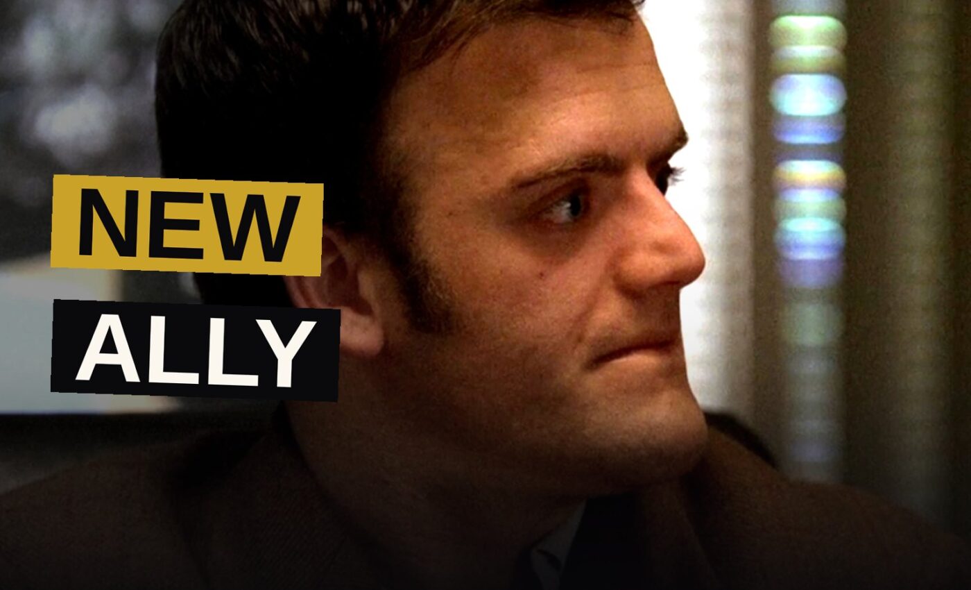 Kevin Weisman as Russell Plum in a dimly lit, cluttered loft, looking determined.