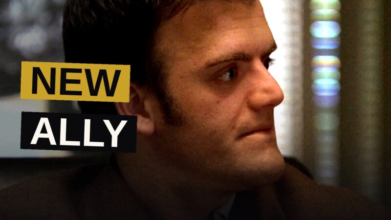 Kevin Weisman as Russell Plum in a dimly lit, cluttered loft, looking determined.