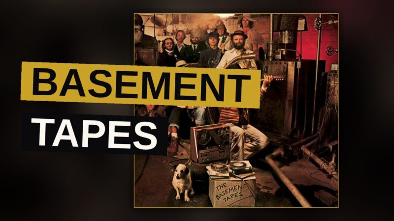 Two musicians play instruments in a dim, cluttered basement, evoking the informal vibe of the Basement Tapes sessions.