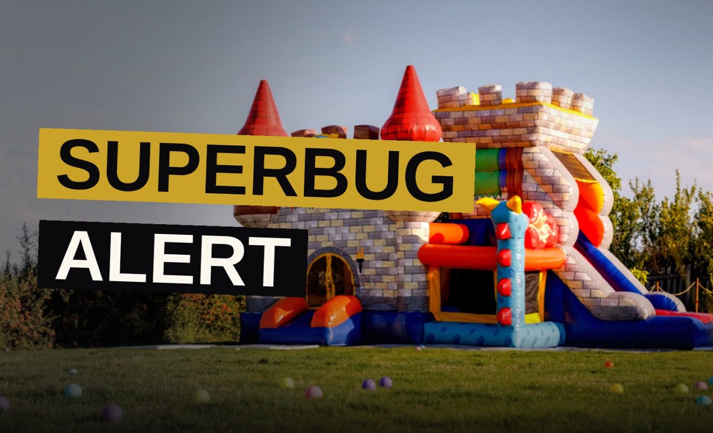 A bouncy castle sits empty on a sunny lawn while tiny shadowy bacteria drift above it.