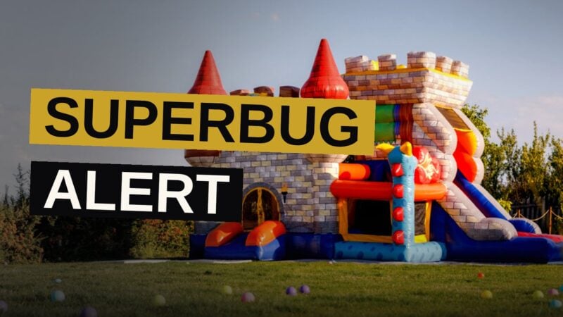 A bouncy castle sits empty on a sunny lawn while tiny shadowy bacteria drift above it.
