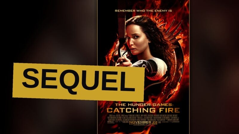 Katniss Everdeen stands in a futuristic arena, bow raised, surrounded by jungle and a glowing force field.