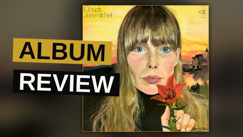 A vintage vinyl record sleeve for Joni Mitchell's 'Clouds' album resting on a wooden table with a guitar nearby.