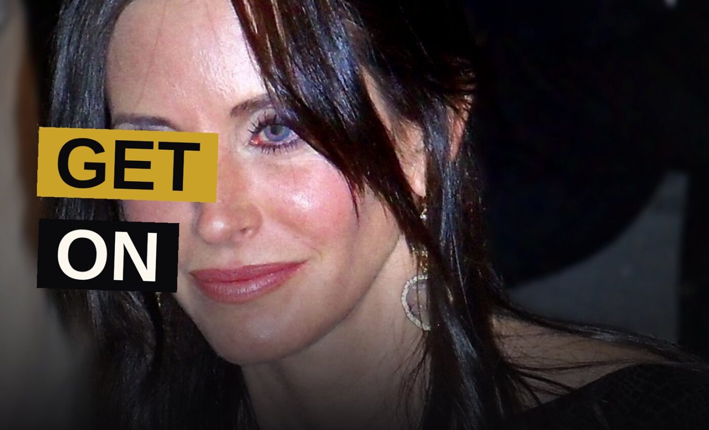 Courteney Cox poses confidently on a festival red carpet with cameras around her.