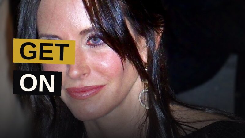 Courteney Cox poses confidently on a festival red carpet with cameras around her.