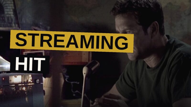 A man stands beside a glowing radio receiver while a ghostly figure of his younger self appears nearby.