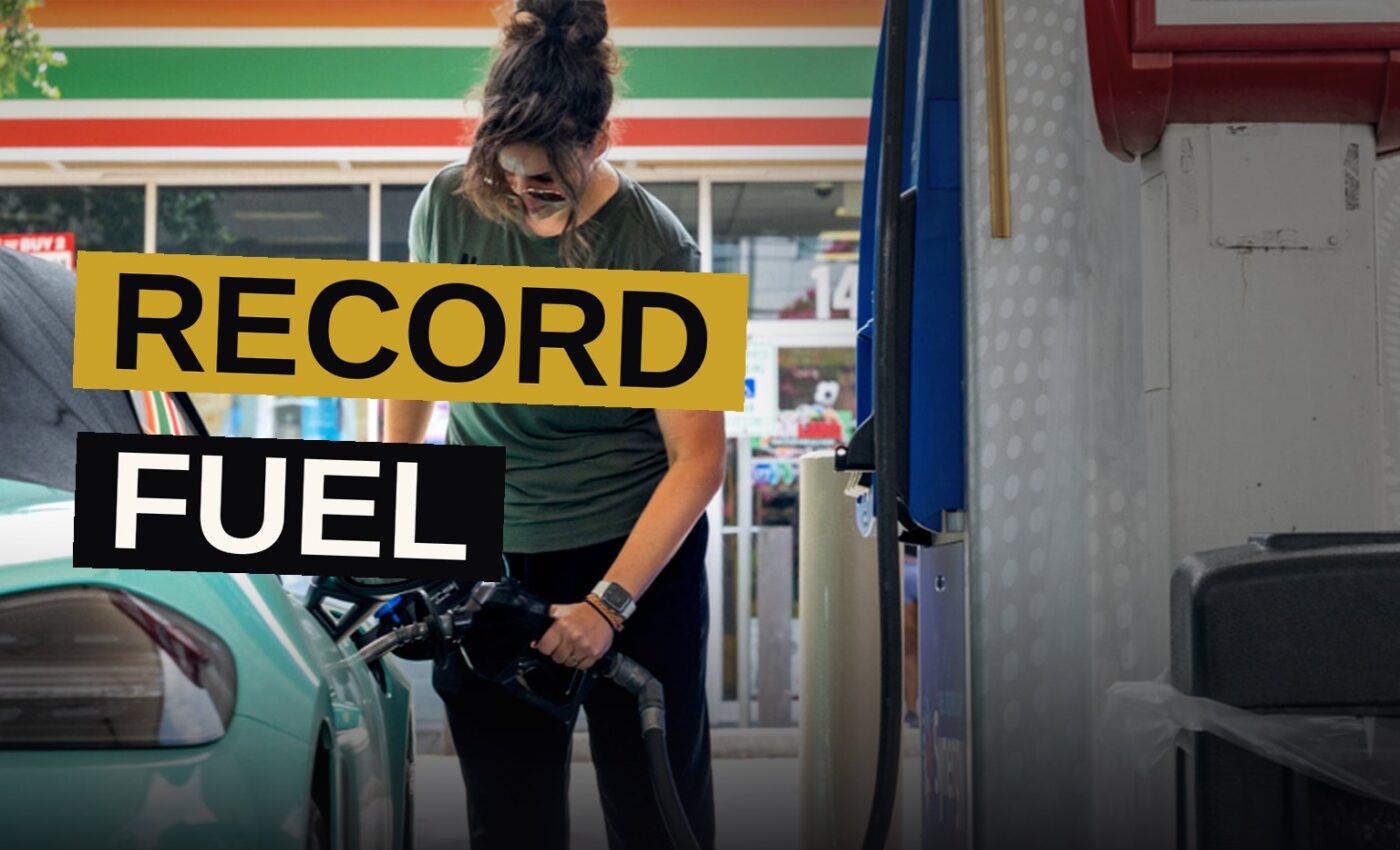 A hand holds a diesel fuel nozzle at a gas station, with a price display showing $5.85 per gallon in the background.