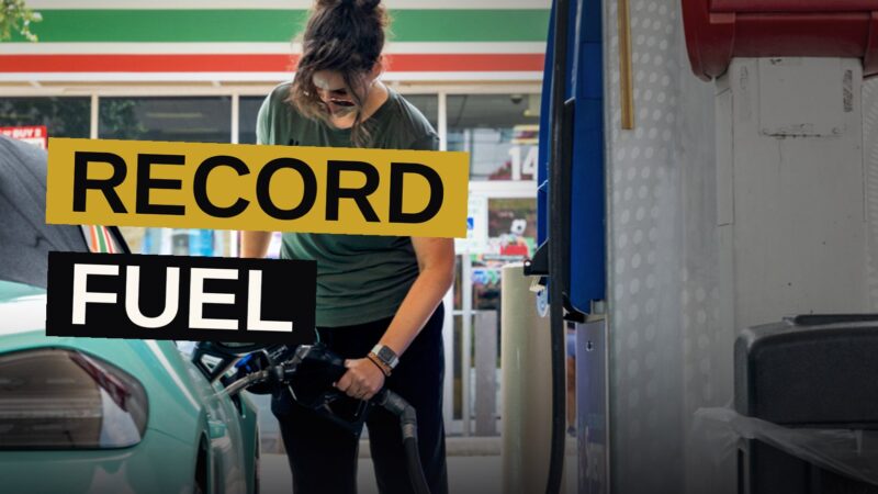 A hand holds a diesel fuel nozzle at a gas station, with a price display showing $5.85 per gallon in the background.