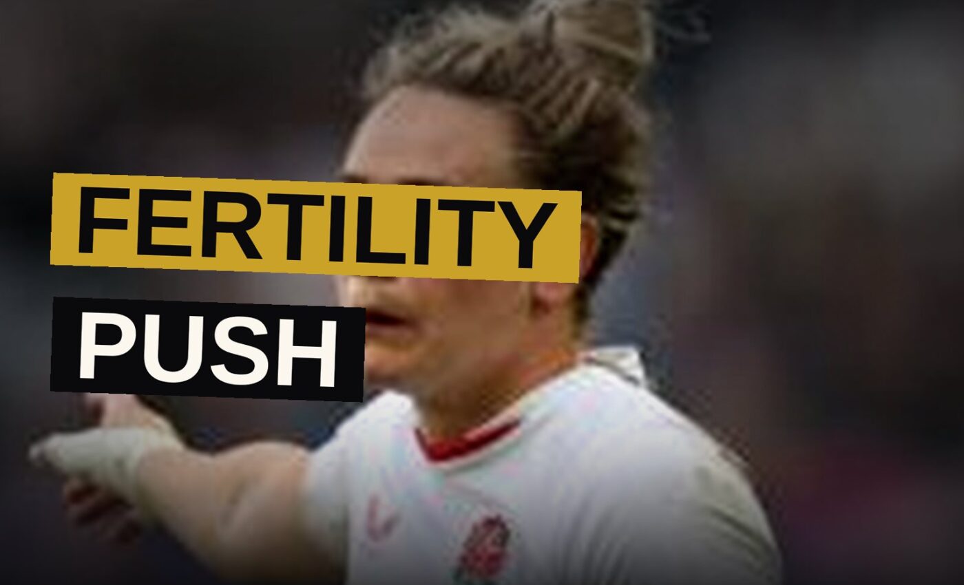 A rugby player stands confidently on a sunlit field, her expression showing determination.