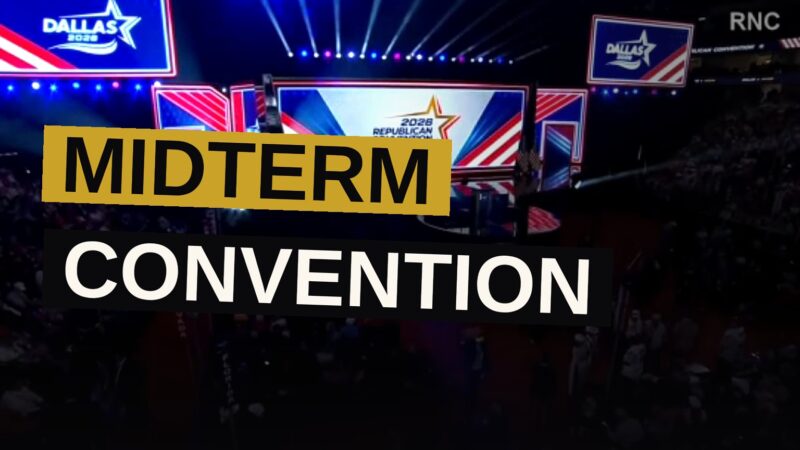 A large convention hall in Dallas with a red, white, and blue stage and a sparse audience.