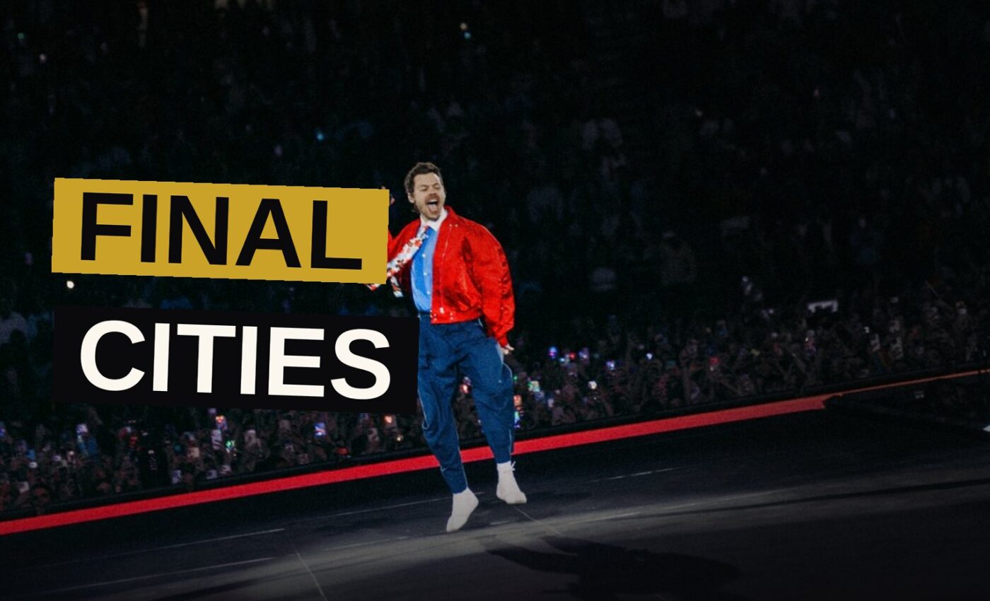 Harry Styles performs on stage during a concert, with fans' hands raised and bright lights illuminating the arena.