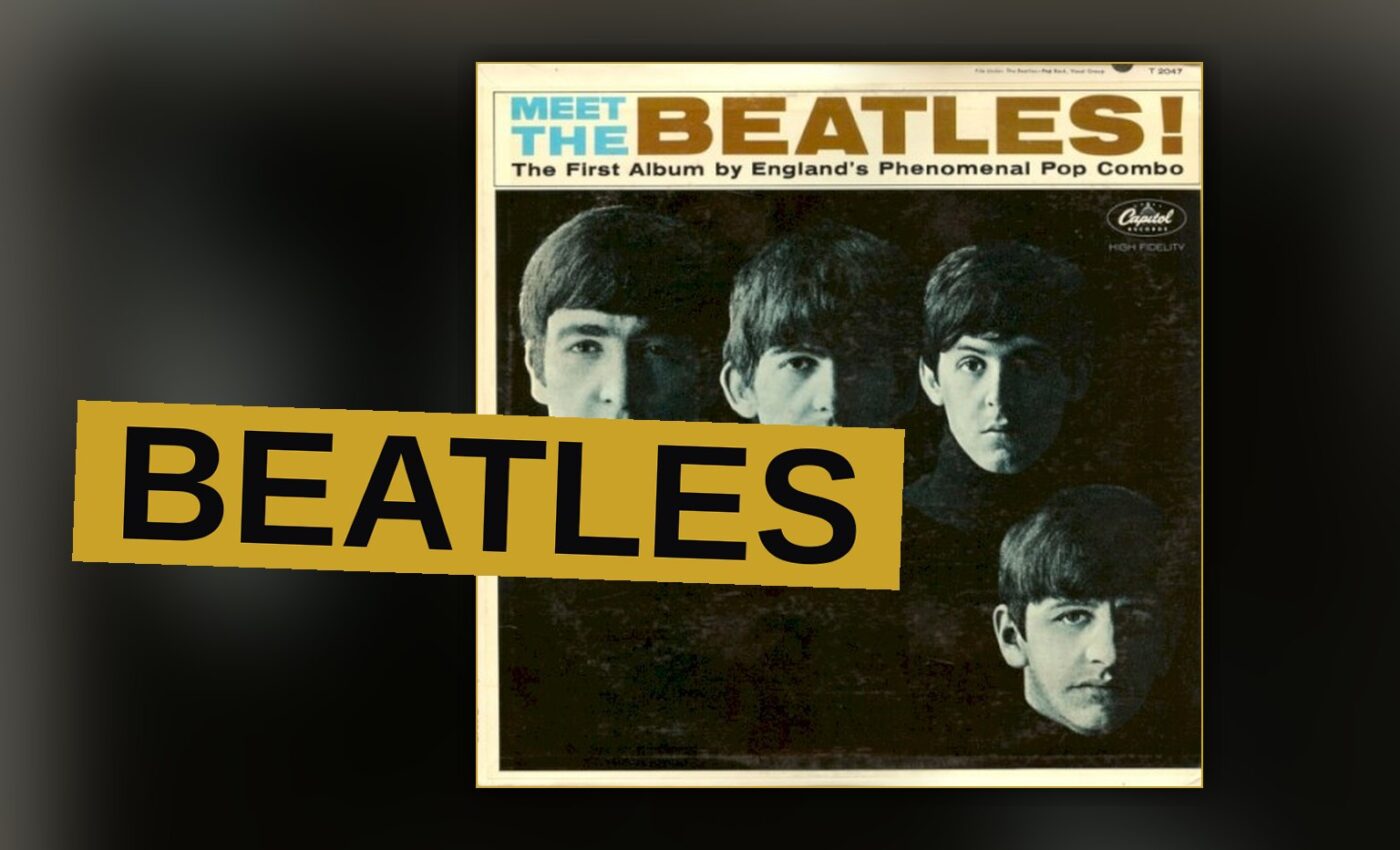 The Beatles posing in matching dark suits with mop-top haircuts, looking at the camera with confident expressions.
