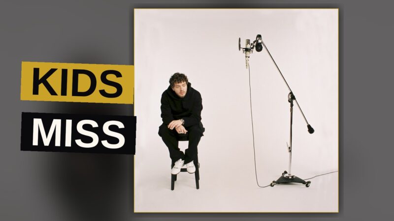 A rapper stands amid dim light and shadow, a solitary figure weighed down by the weight of fatherhood and fame.