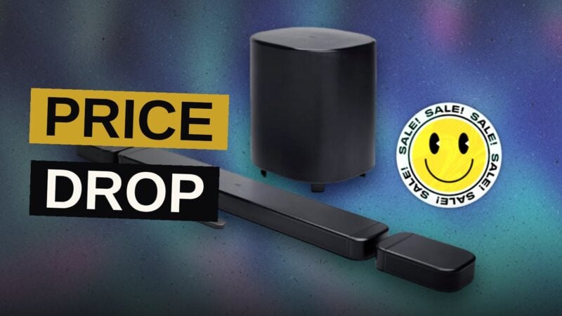 A dark soundbar rests beneath a glowing television, its wireless companions set apart upon the floor.
