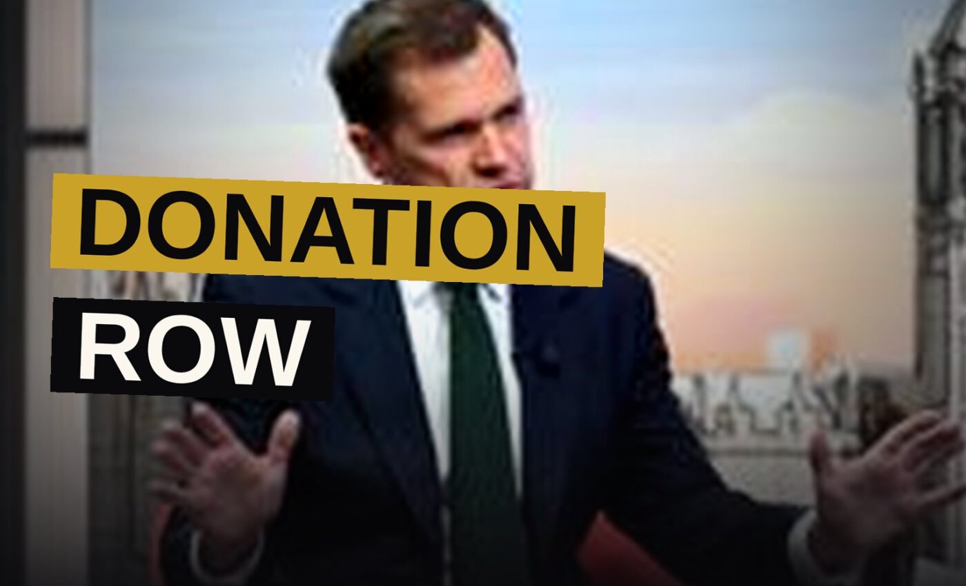 A politician speaks at a press conference with a large screen displaying the figure '£72m' behind him.