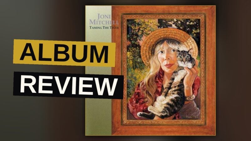 Joni Mitchell plays an acoustic guitar in a dimly lit studio, her expression contemplative and the lighting warm and soft.