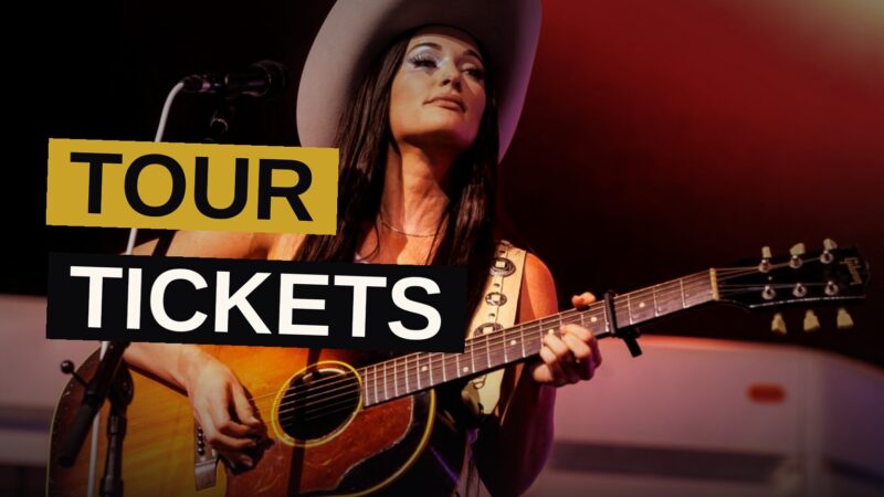 Kacey Musgraves performs on stage under colorful lights with a large disco ball behind her, as fans raise their hands in the crowd.