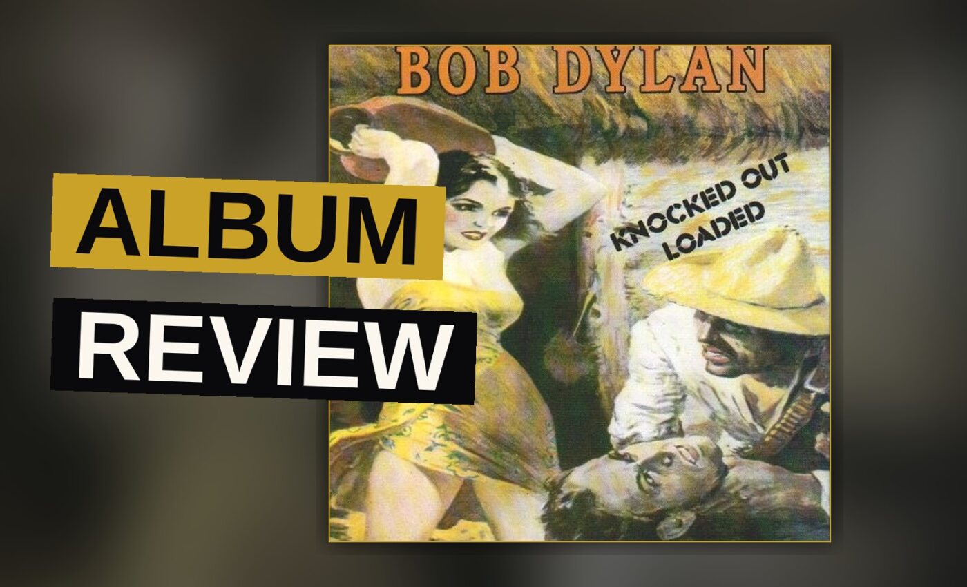 A vintage cassette tape of Bob Dylan's album Knocked Out Loaded rests on a wooden table in a dimly lit room.