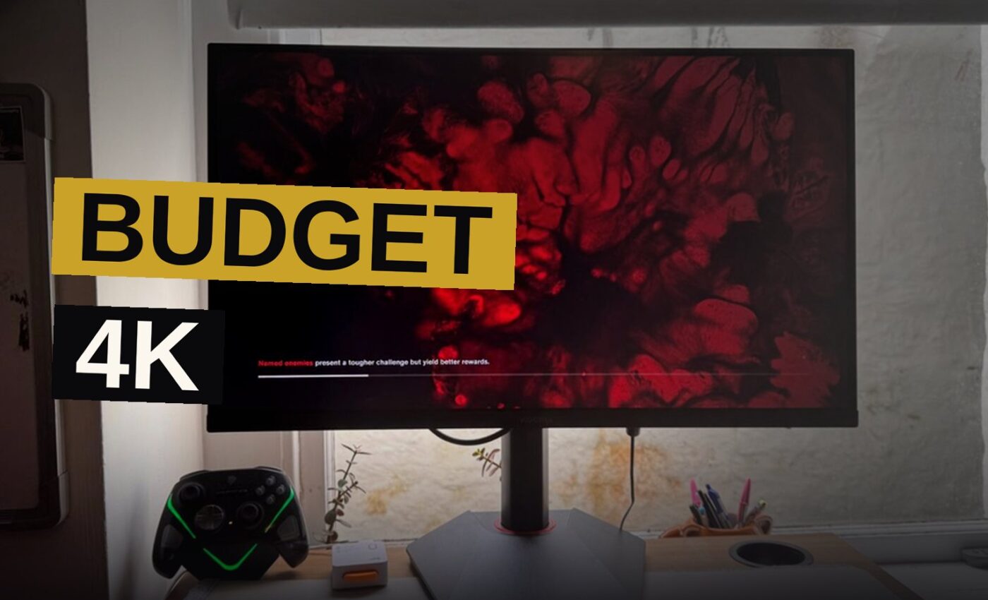 A Koorui G2741L gaming monitor on a desk showing a colorful 4K game scene, with a window and soft light nearby.