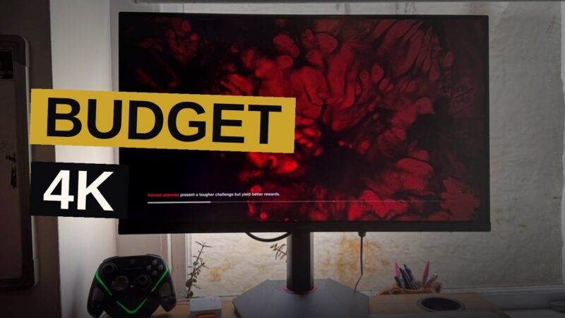 A Koorui G2741L gaming monitor on a desk showing a colorful 4K game scene, with a window and soft light nearby.