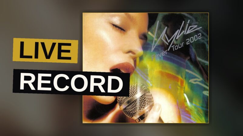 Kylie Minogue performs energetically on a grand arena stage lit with vibrant neon lights.
