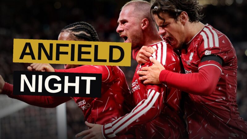Liverpool players in red react after scoring a goal at Anfield during a night match.