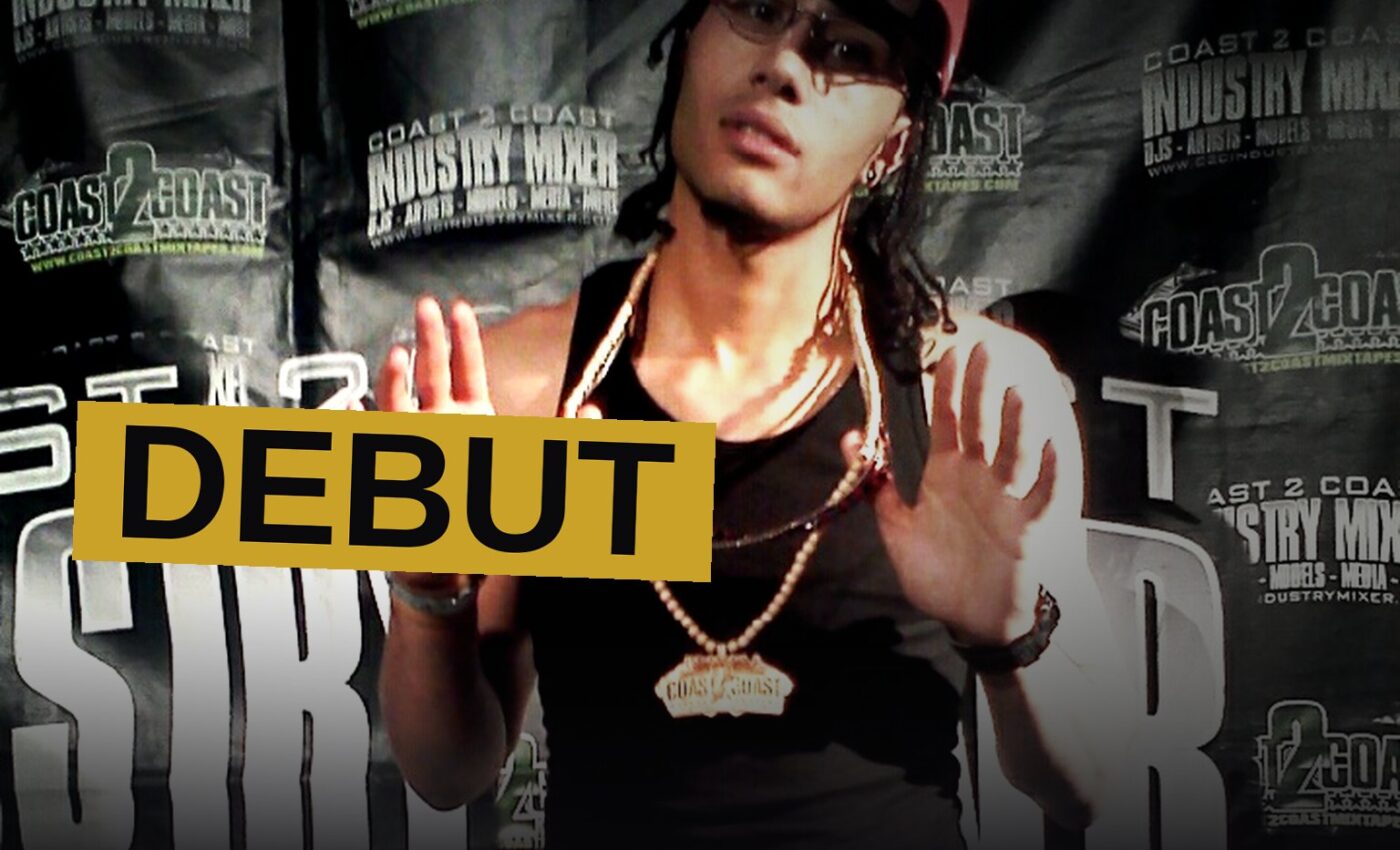 A young rapper stands in a dim room surrounded by vinyl records, evoking the era of his debut album.