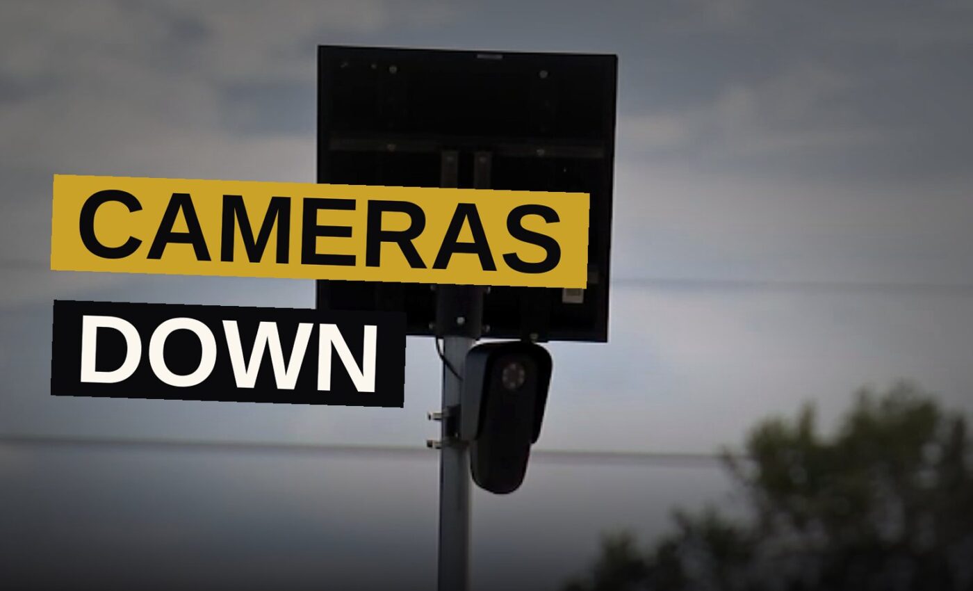 Workers remove a license-plate camera from its post while the street lies quiet in the gathering dusk.
