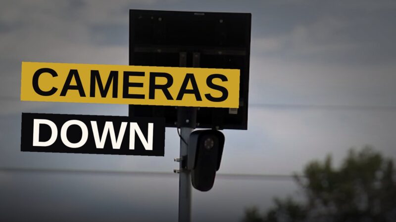 Workers remove a license-plate camera from its post while the street lies quiet in the gathering dusk.