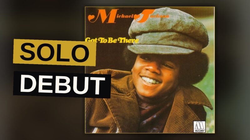 A young Michael Jackson with an afro sings into a retro microphone in a warm, sepia-toned 1970s studio setting.