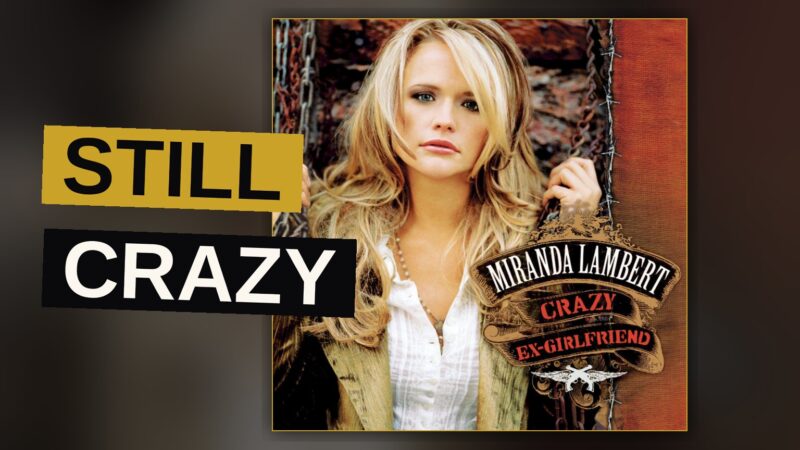 A female country singer performs energetically on a dark stage lit with red and blue lights.