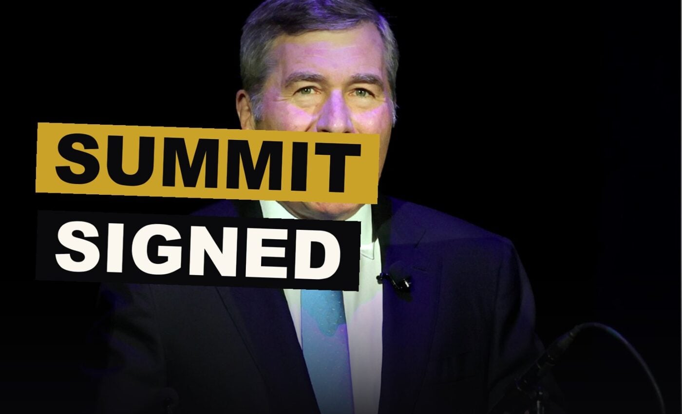 Leaders and studio chiefs sit together at a table, signing papers beneath banners of the summit.