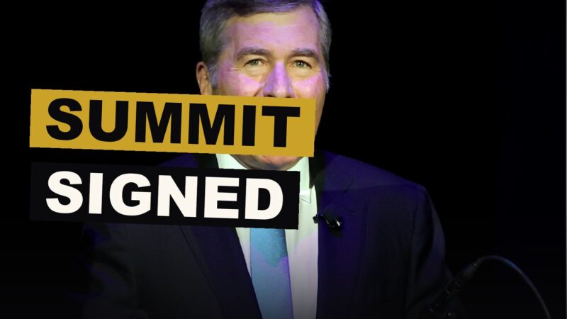 Leaders and studio chiefs sit together at a table, signing papers beneath banners of the summit.