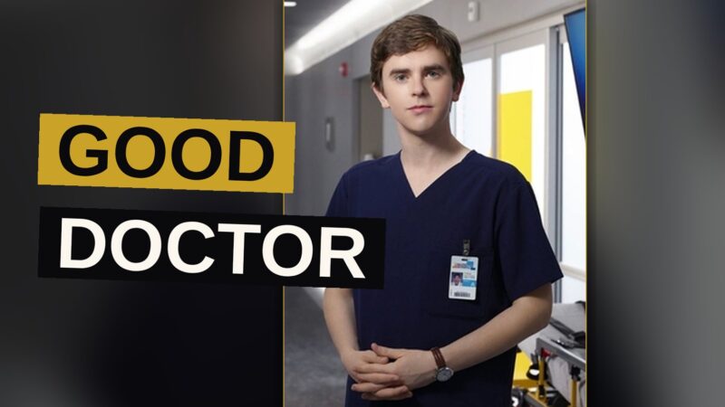A young man dressed in a white coat stands in a dimly lit hospital hallway.