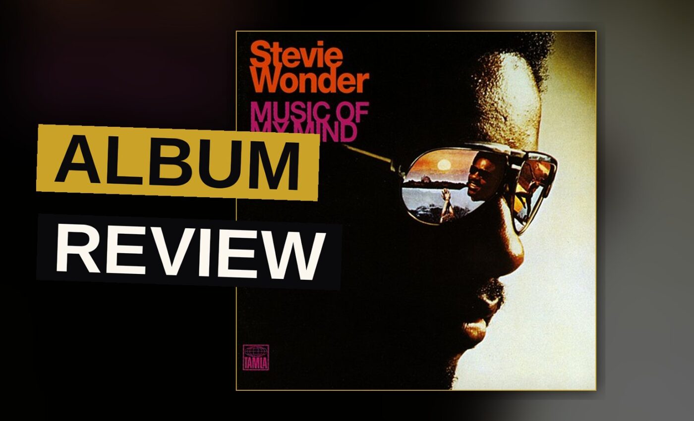 A young Stevie Wonder in the 1970s, smiling, surrounded by keyboards and synthesizers in a recording studio.
