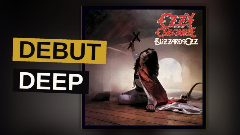 A singer stands alone on a dimly lit stage bathed in red and blue light, evoking the theatrical mood of the album.