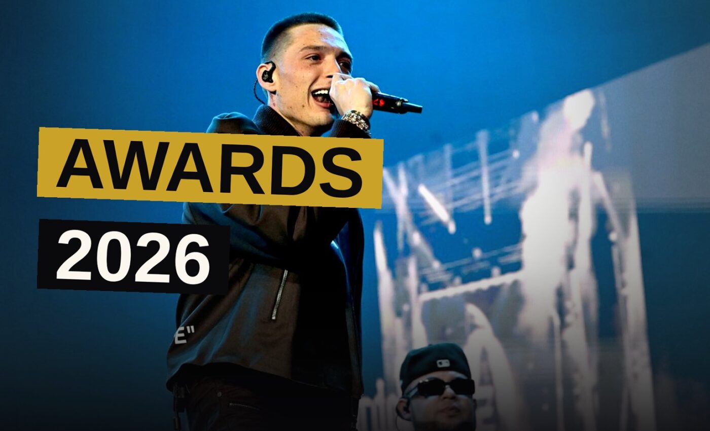 A singer performs on a brightly lit award show stage with golden light beams.