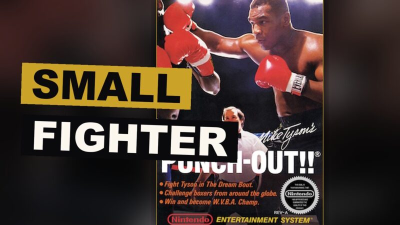 A small boxer squares off against a towering foe beneath the light of a solitary lamp within the ring.