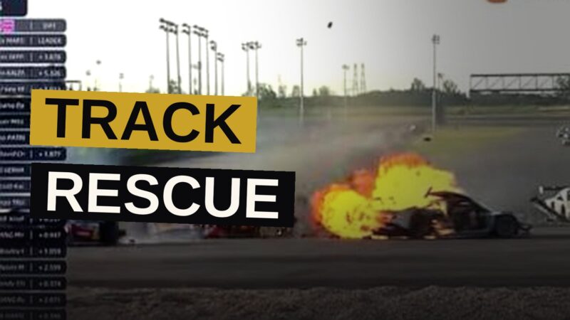 A driver, with singular courage, draws a fellow racer from the fiery wreck of his burning car upon the track.