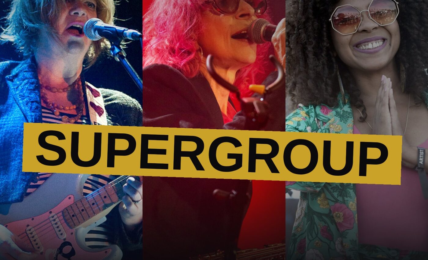 Three punk rock women perform together on a dark stage with guitars.