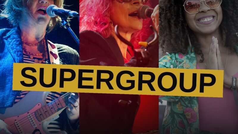 Three punk rock women perform together on a dark stage with guitars.