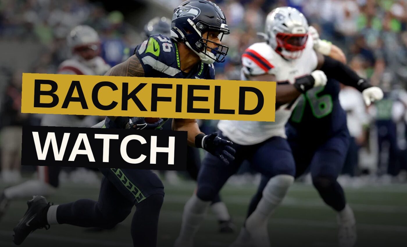 A Seattle Seahawks running back carrying the football during a game, with the stadium blurred in the background.