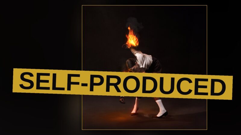 A silhouetted performer stands amid smoke and stage lights in a raw, industrial studio setting.