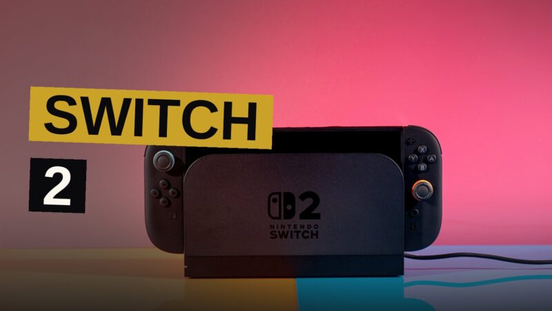 A Nintendo Switch 2 console in its dock connected to a large TV, with a colorful game displayed on the screen in a bright living room.