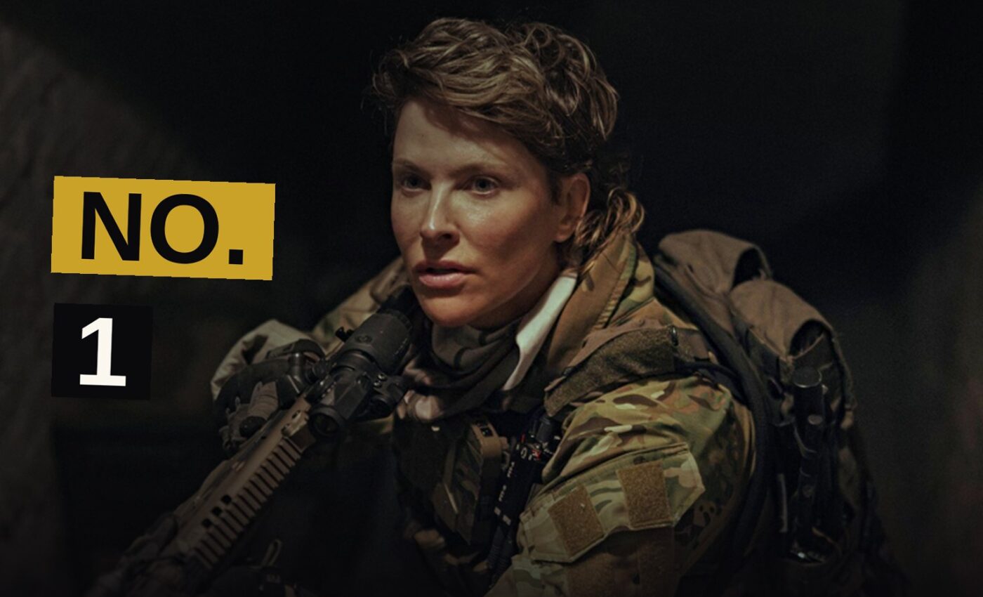 A tense female CIA operative stands watchful in a shadowy urban setting.
