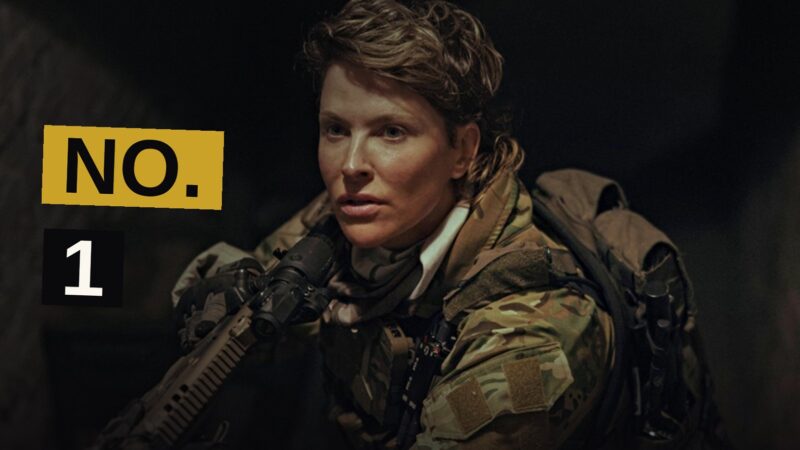 A tense female CIA operative stands watchful in a shadowy urban setting.