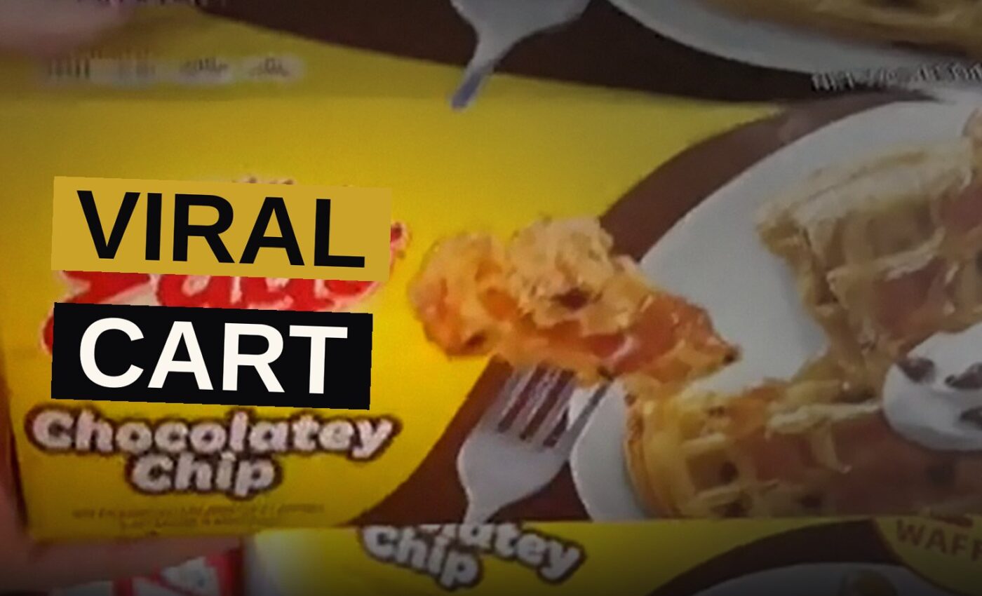 A grocery cart filled with processed foods sits in a supermarket aisle.